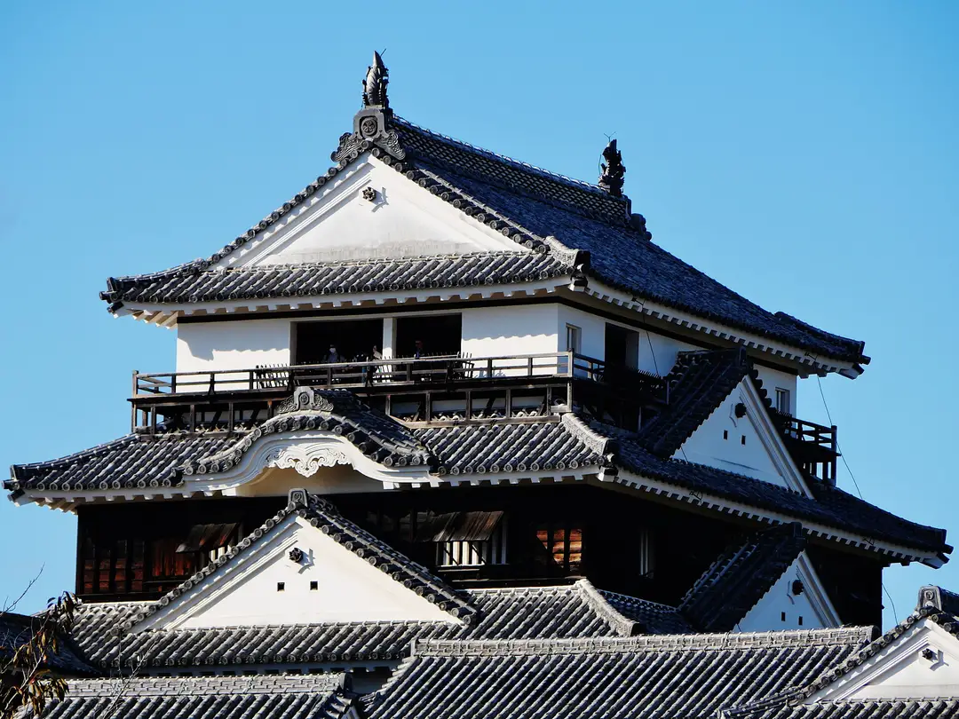 The original wooden keep of Matsuyama Castle, its layered white walls and black-tiled gables against a clear blue sky, Ehime