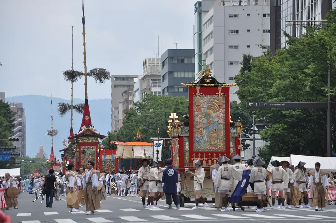 Two great Gion Matsuri floats pulled along a Kyoto avenue by teams of haulers during the Yamaboko Junko procession, hills behind