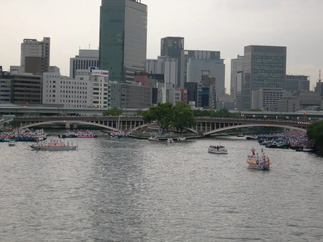 Boats of the Tenjin Matsuri river procession moving along the Okawa past the Osaka skyline and a bridge